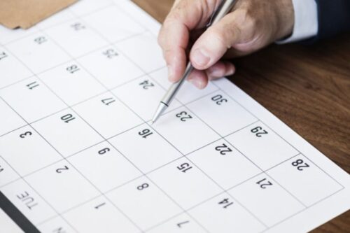 Pessoa marcando uma data no calendário com uma caneta.