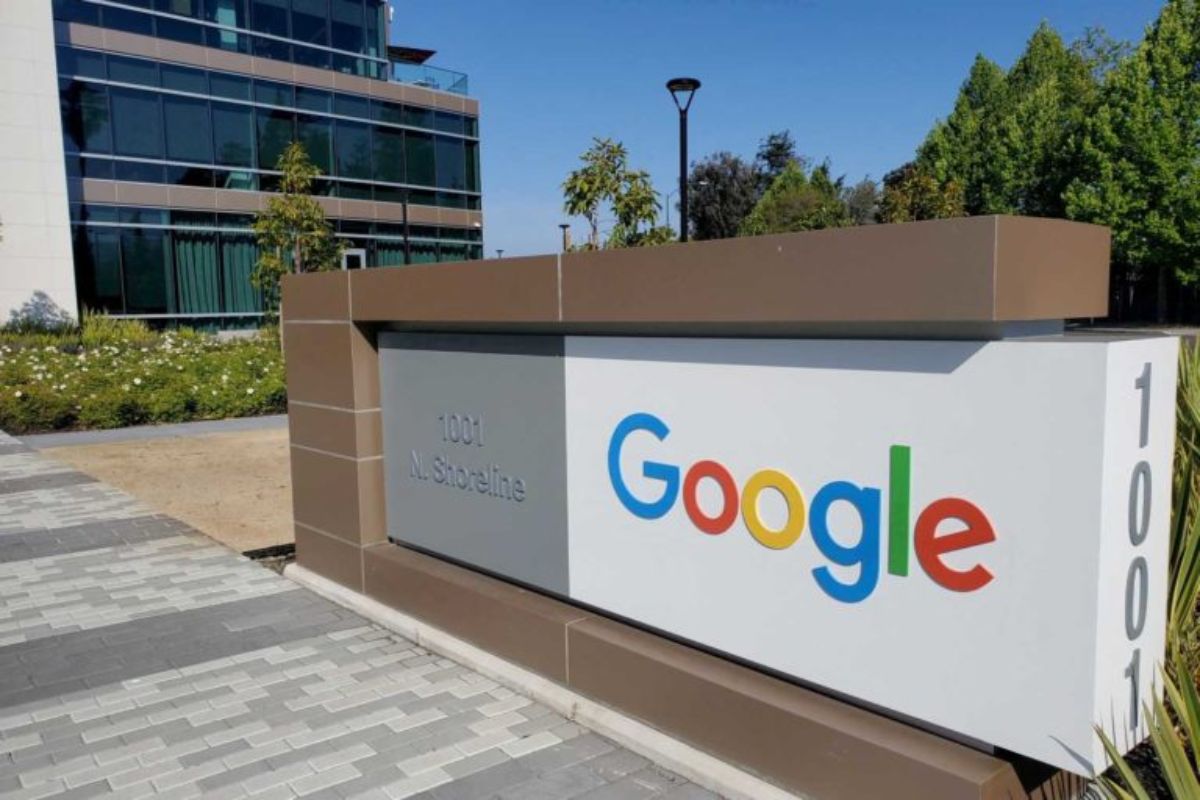 Placa na entrada do Google em Mountain View, Califórnia, com destaque para o logotipo colorido da empresa e uma fachada moderna ao fundo.