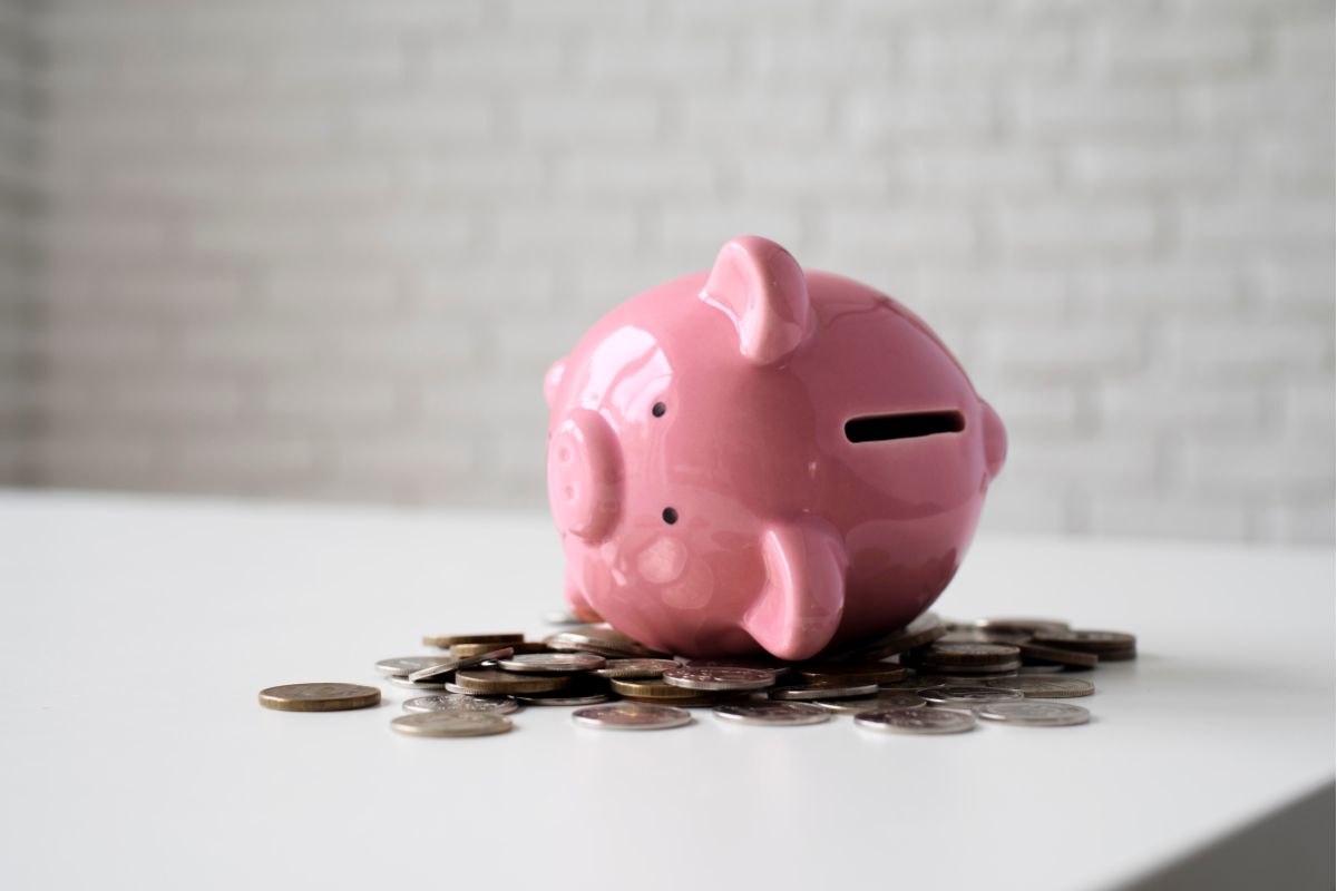 Porquinho piggy bank rosa com moedas de dinheiro sobre uma mesa branca, simbolizando economia e poupança.