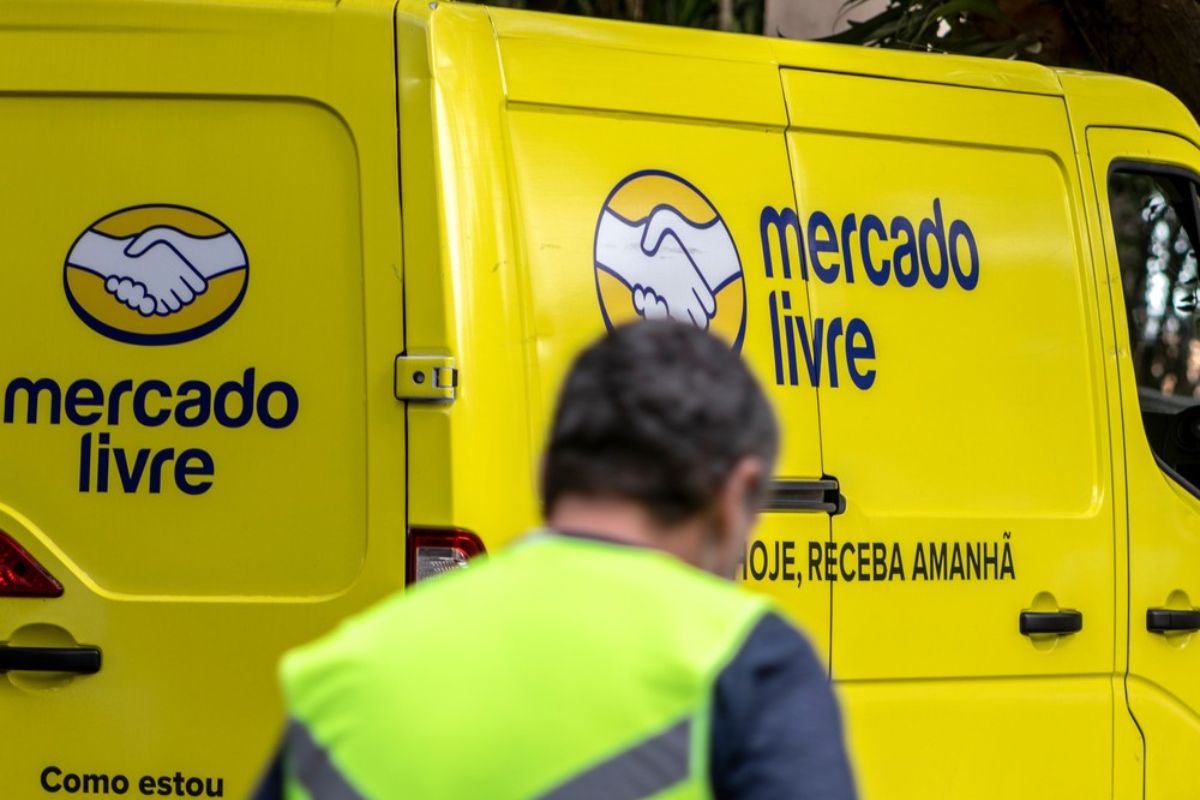 Pessoa de costas usando colete refletivo em frente a uma van amarela do Mercado Livre, com logo e slogan visíveis.