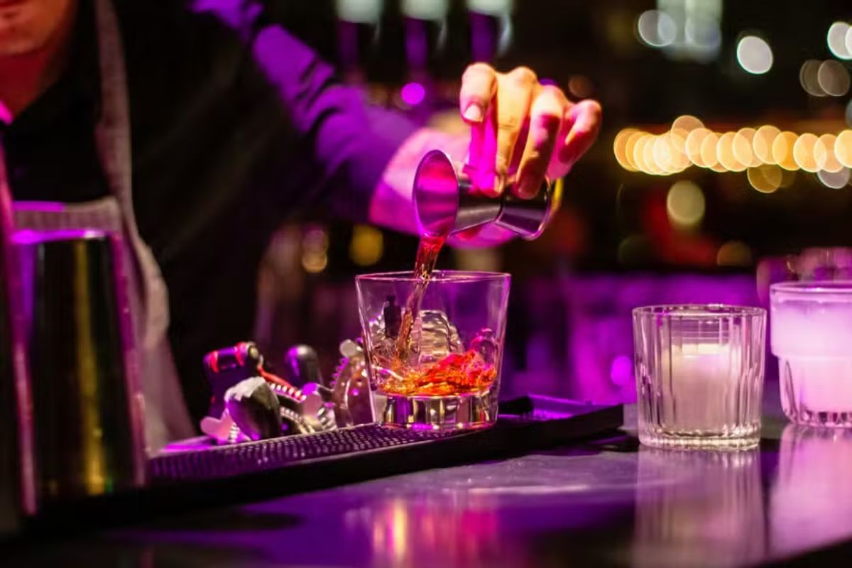 Barman preparando um drink em bar com iluminação colorida e ambiente sofisticado