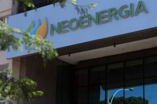 Fachada do edifício NeoEnergia com o logotipo e sinalização visível, refletindo iluminação natural e um ambiente corporativo sustentável.