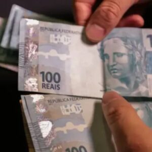 Pessoa segurando notas de 100 reais, dinheiro em cédulas brasileiras, com destaque para as características das notas.