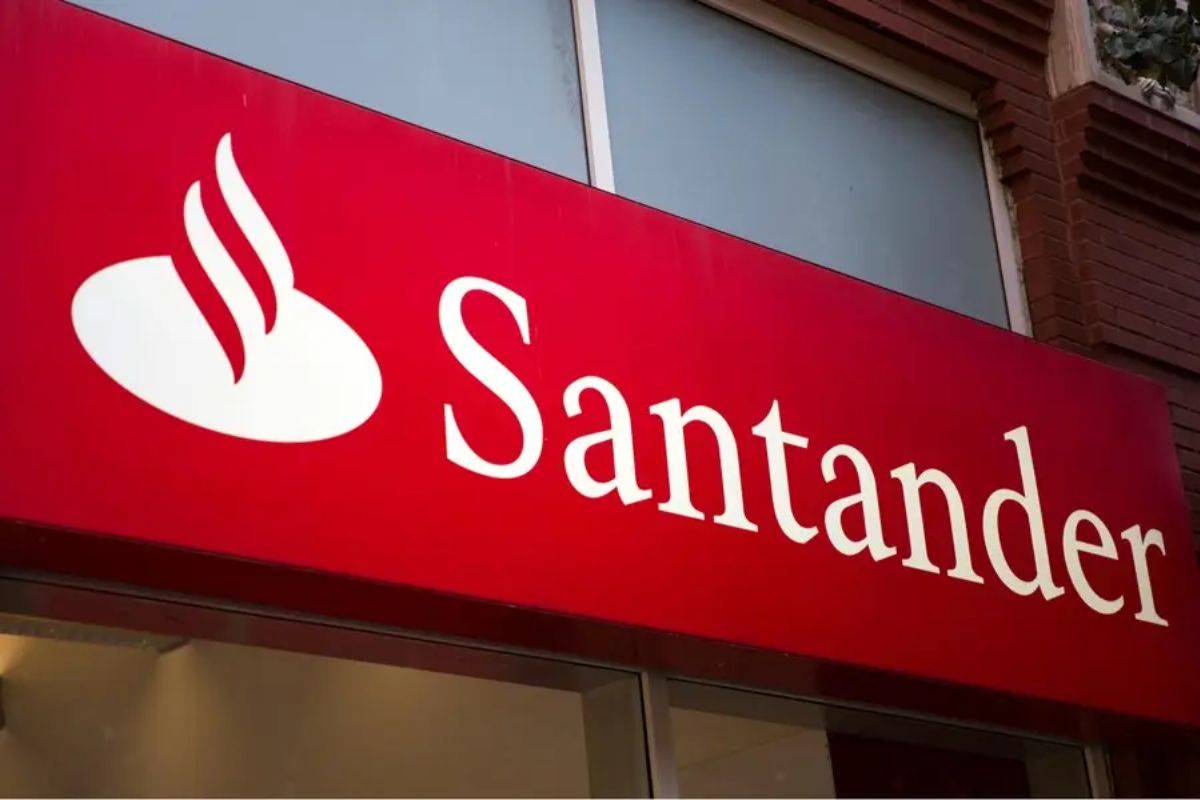 Loja do banco Santander com logotipo vermelho e branco, destaque para o nome Santander e símbolo de uma folha de bordo estilizada, em ambiente urbano.