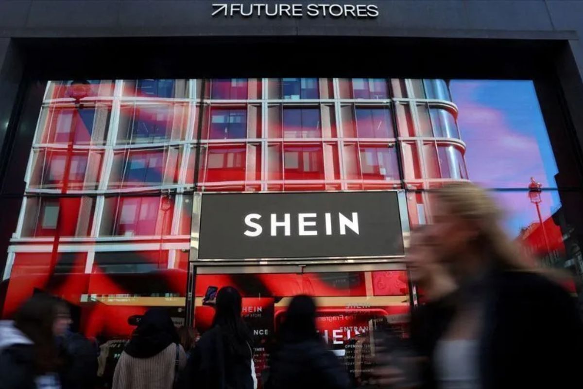 Fachada da loja Shein em um shopping comexternas modernas, vidro refletivo e pessoas passando em frente, destacando a marca Shein e a fachada futurista.
