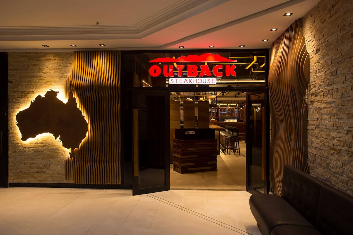 Entrada iluminada de um restaurante Outback Steakhouse, usada em artigo sobre quem é o dono do Outback Steakhouse.