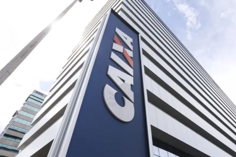 Vista em ângulo de um prédio de escritórios alto e moderno com o logotipo 'CAIXA' em letras grandes e brancas sobre um painel azul marinho.