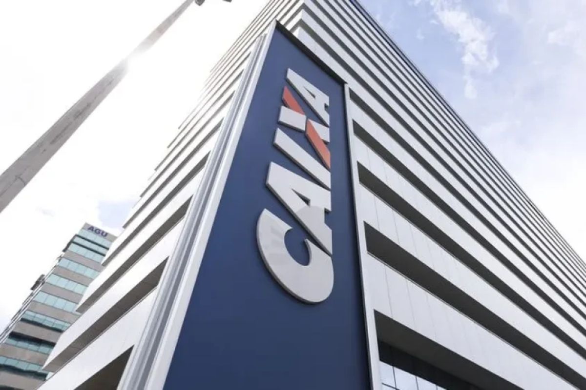 Vista em ângulo de um prédio de escritórios alto e moderno com o logotipo 'CAIXA' em letras grandes e brancas sobre um painel azul marinho.