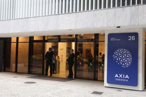 Fachada moderna de um edifício em uma área urbana, com uma placa de sinalização azul e branca proeminente ao lado da entrada principal.