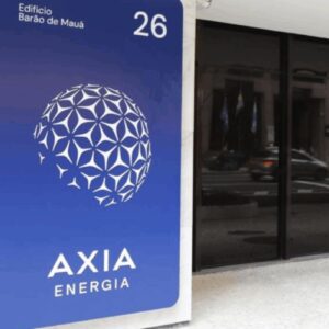Placa de identificação da empresa Axia Energia fixada em uma coluna de mármore na entrada de um edifício. A placa é azul escura e exibe o logo da empresa (uma esfera geométrica branca), o nome "AXIA ENERGIA" e o endereço "Edifício Barão de Mauá 26" em letras brancas. Ao fundo, vê-se uma fachada de vidro escuro.