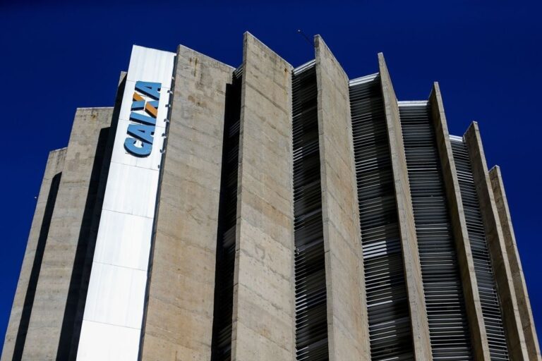 Vista angular do Edifício Sede da Caixa Econômica Federal, em Brasília. O prédio de arquitetura brutalista é alto, tem fachadas de concreto e pilares verticais que se projetam, e exibe o logo azul e laranja da 'CAIXA' em uma placa vertical branca na lateral.