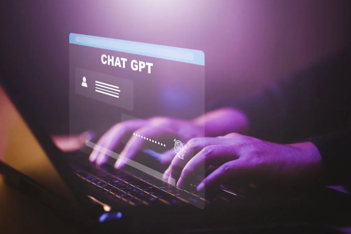 Mãos digitando em um teclado de notebook com luzes roxas, e uma tela de interface virtual de "CHAT GPT" flutuando acima.