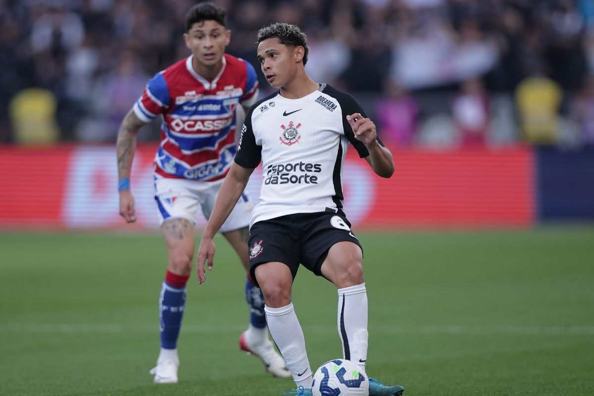 Dieguinho em ação durante partida, concentrado na bola, com adversário ao fundo em estádio cheio, usando uniforme do time Corinthians.