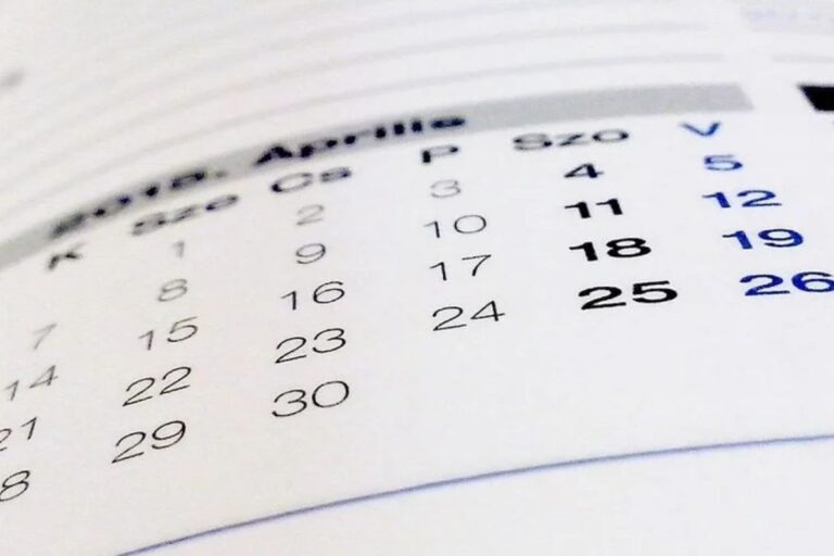 Uma visão em close-up e desfocada de um calendário em papel, mostrando os dias e números de um mês, provavelmente 'Abril' ou 'Aprilie', com os números 18, 19 e 25 destacados em negrito.