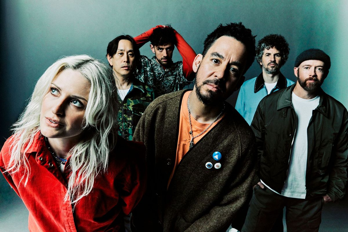 Foto em estúdio de close-up da nova formação da banda Linkin Park. Em primeiro plano, no lado esquerdo, está a vocalista Emily Armstrong, loira e de camisa vermelha. No centro, ligeiramente mais atrás, está Mike Shinoda, de barba, casaco marrom e camiseta laranja. Ao fundo, estão os outros membros da banda: Joe Hahn (de camisa verde camuflada), Colin Brittain (de camisa vermelha levantada atrás da cabeça), Dave 'Phoenix' Farrell (de camisa azul clara) e Brad Delson (de gorro escuro e casaco verde militar).