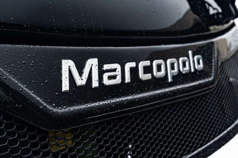 Logo do carro Marcopolo em uma grade dianteira com gotas d'água, em close-up, realçando detalhes e textura.