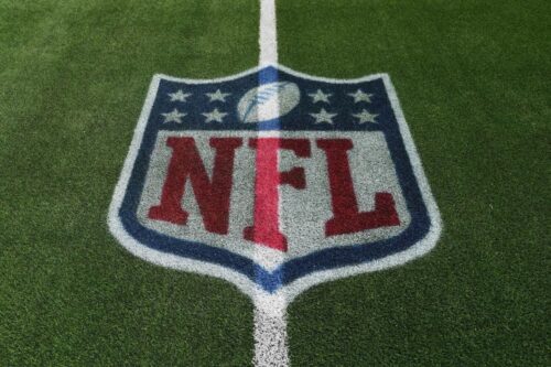 Logotipo da NFL (National Football League) pintado no centro de um campo de grama artificial verde, com as cores vermelho, branco e azul.