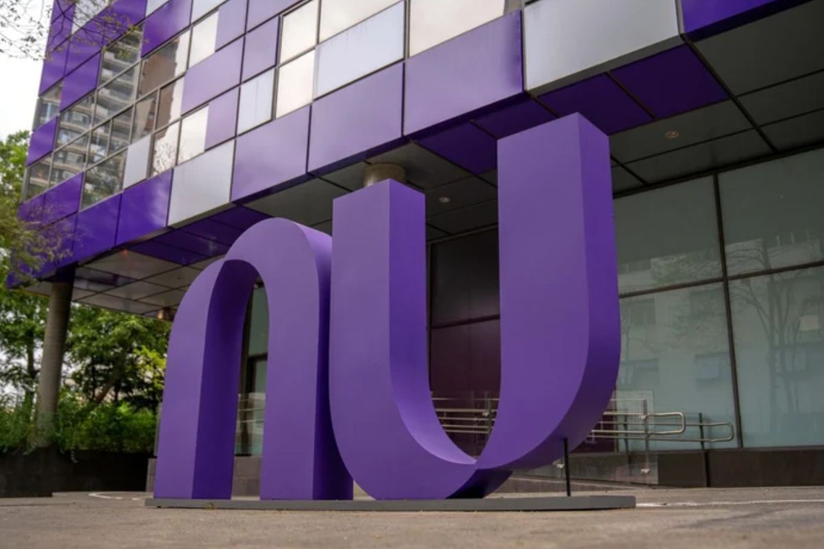 Uma escultura grande e roxa das letras 'nu', o logotipo da Nubank, em frente ao edifício de escritórios da empresa, que também tem detalhes em roxo e espelhado.