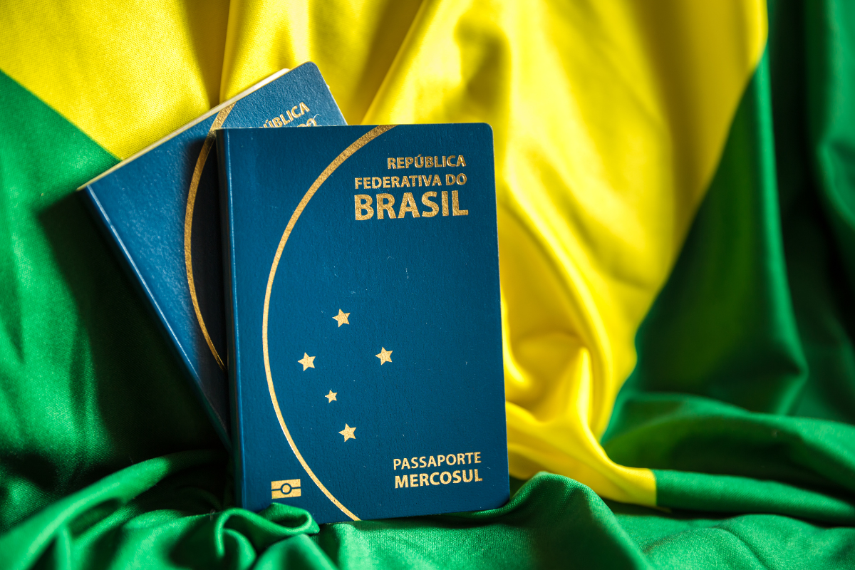 Passaporte da República Federativa do Brasil em destaque sobre uma bandeira do Brasil, com cores verde, amarelo e azul ao fundo.