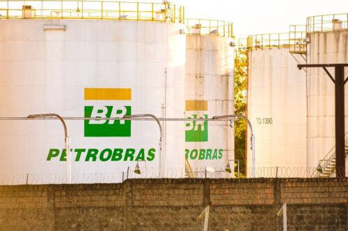 Grandes tanques de armazenamento de combustível, brancos e cilíndricos, com o logotipo da Petrobras (BR verde e amarelo) pintado em suas laterais.