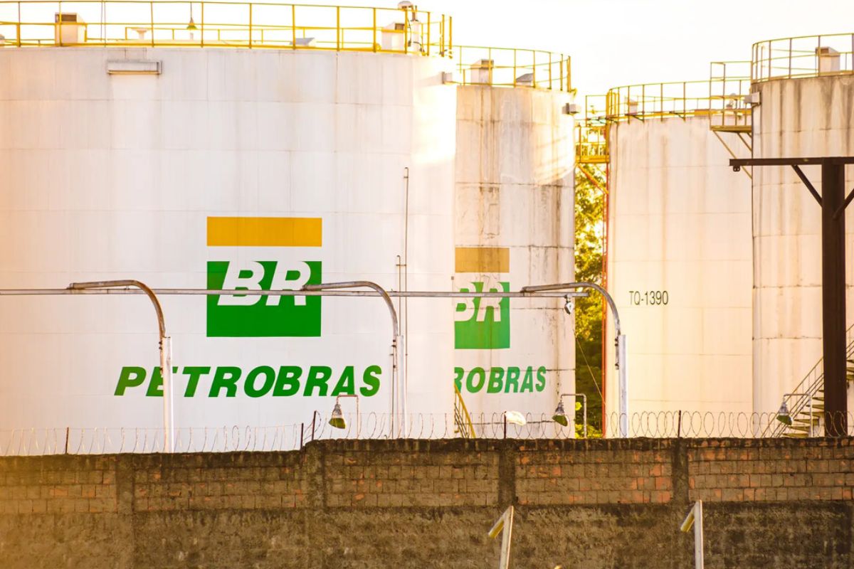 Grandes tanques de armazenamento de combustível, brancos e cilíndricos, com o logotipo da Petrobras (BR verde e amarelo) pintado em suas laterais.