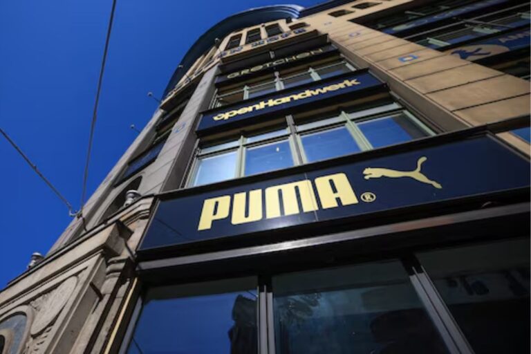 Vista de baixo para cima da fachada de um prédio comercial em um dia de céu azul, destacando a placa preta da loja PUMA.