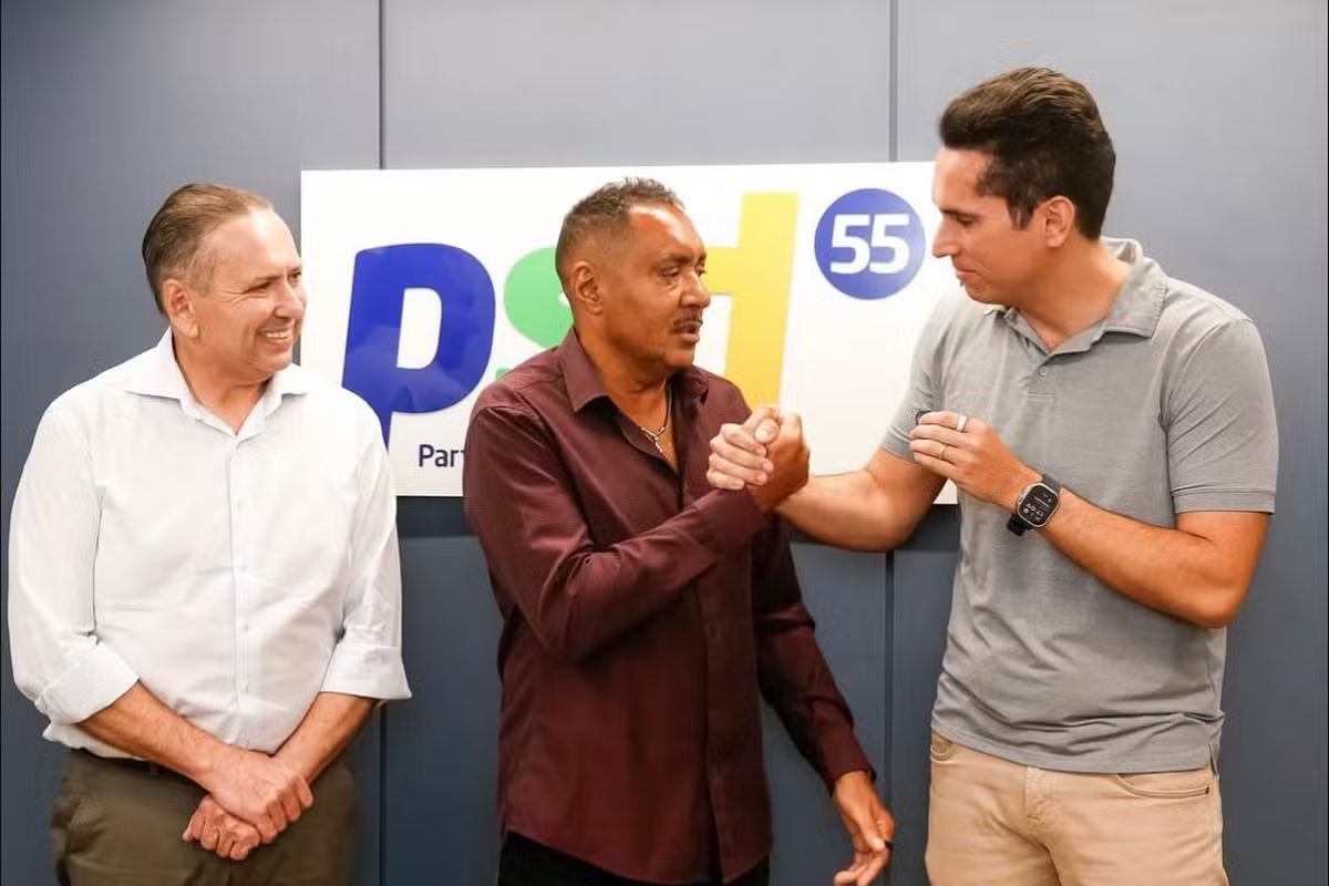 Momento da filiação política do deputado Tiririca ao PSD. Tiririca (camisa vinho) aperta as mãos de um líder partidário em frente ao painel com o logotipo 'PSD 55', celebrando sua adesão ao partido no Ceará.