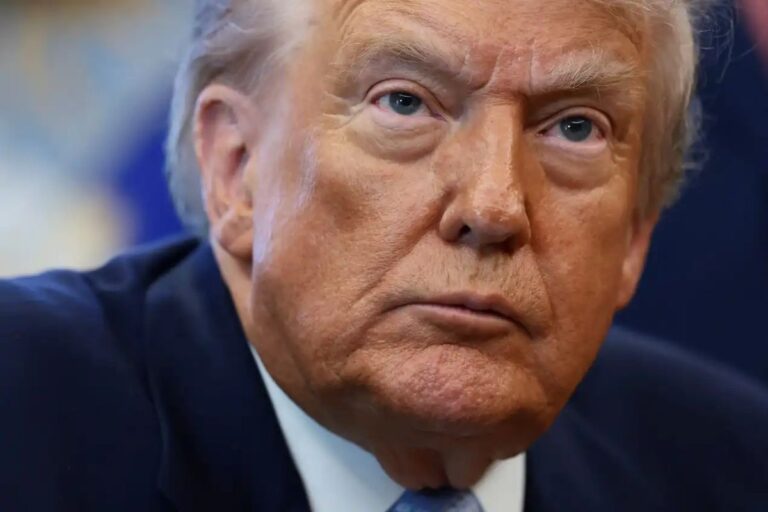 Close-up extremo do rosto de Donald Trump. Ele veste um terno escuro e uma gravata, e olha diretamente para a frente com uma expressão séria e concentrada.