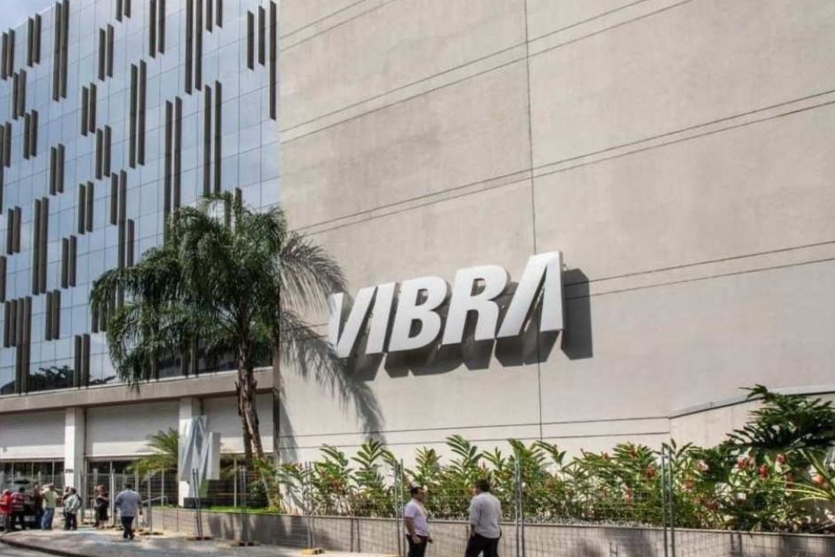 O logotipo "VIBRA" em letras grandes e brancas está fixado na fachada de um edifício comercial moderno e claro.