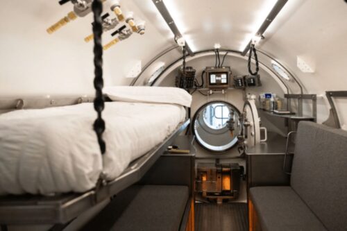 Interior de um espaço confinado e cilíndrico, semelhante a um submersível ou câmara de descompressão.