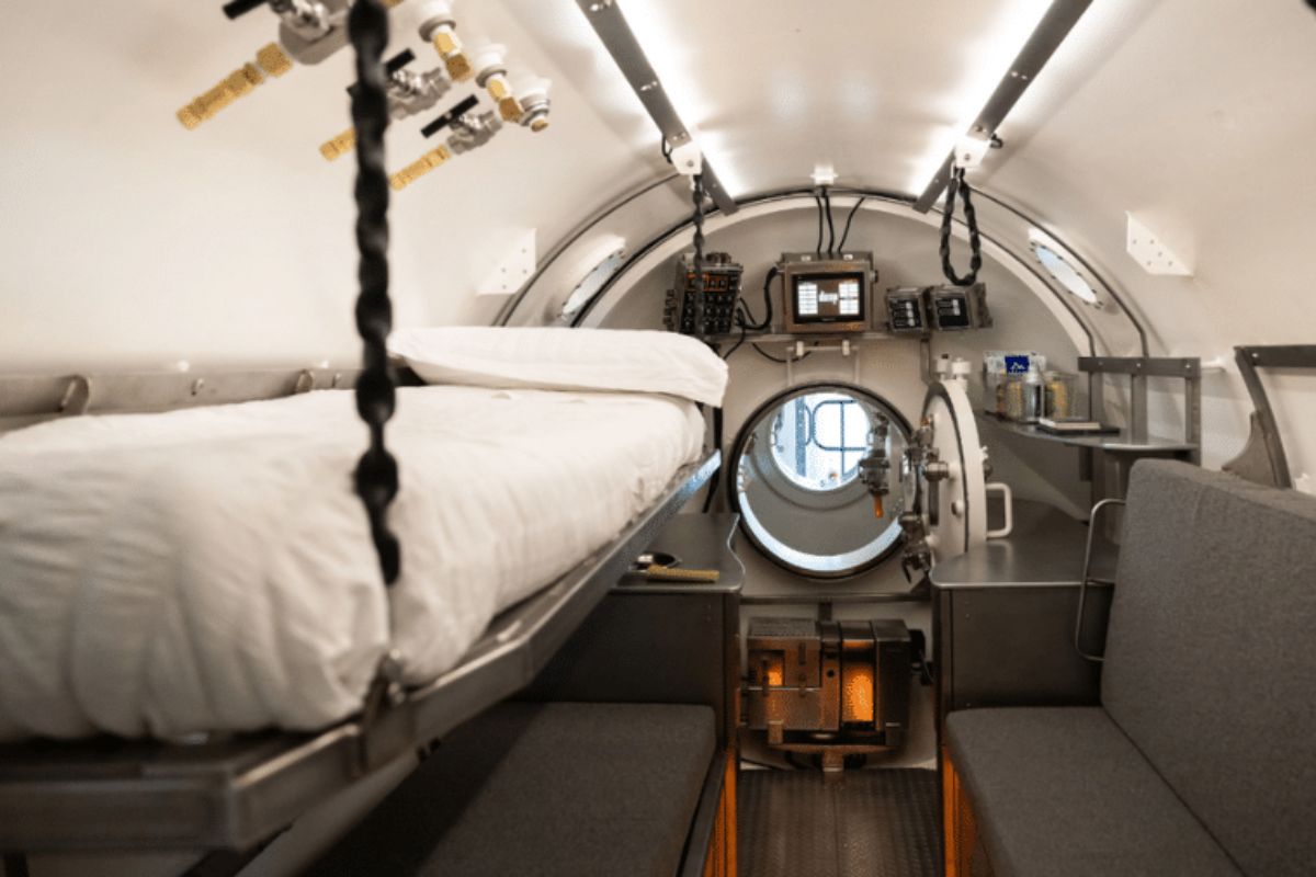 Interior de um espaço confinado e cilíndrico, semelhante a um submersível ou câmara de descompressão.