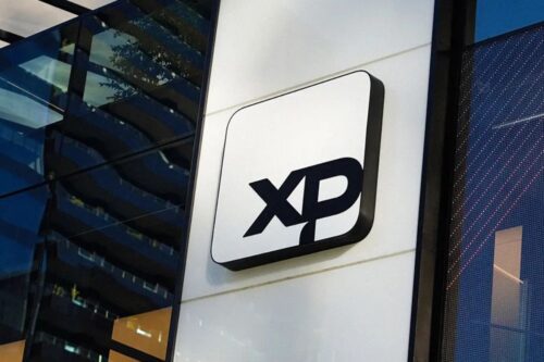 Placa com o logotipo preto da XP montada na fachada externa de um edifício moderno