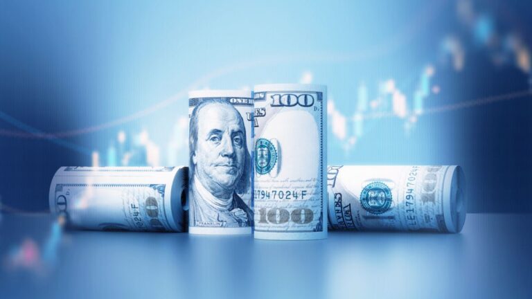 Notas de dólar americano enroladas sobre fundo azul, representando a cotação do dólar em queda no mercado financeiro.