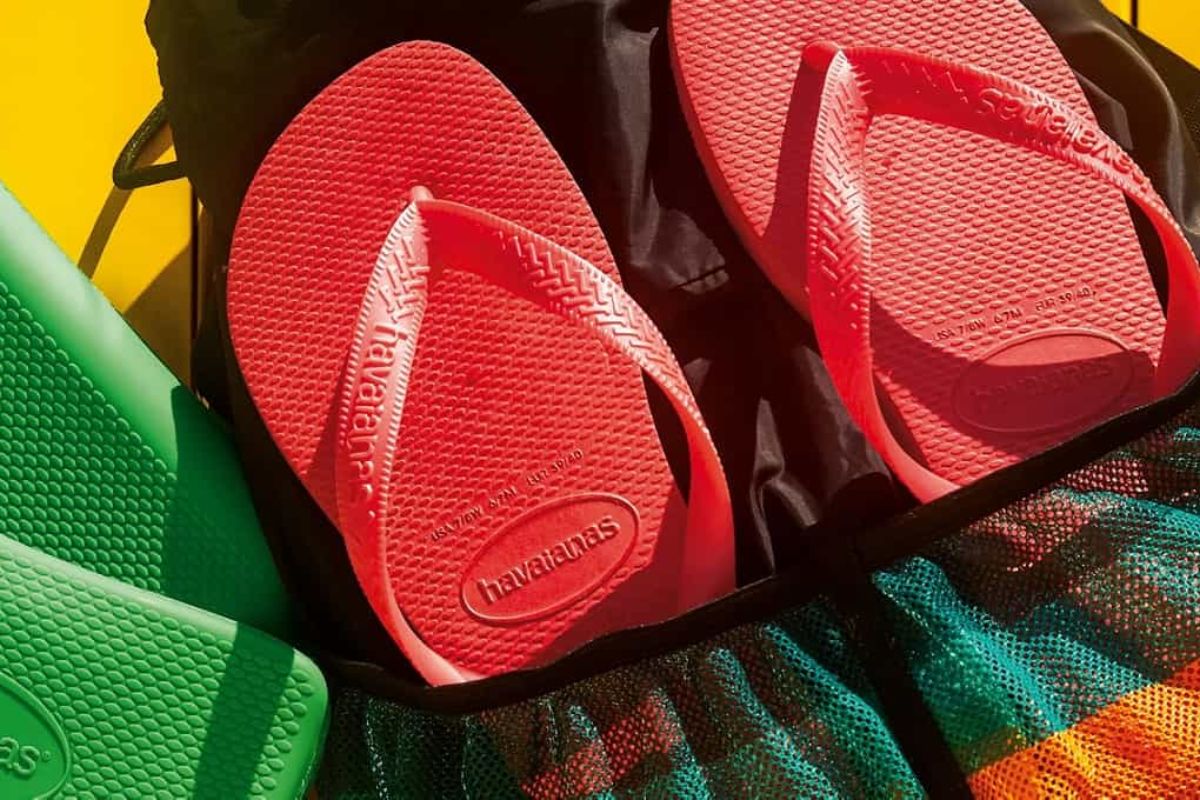 Um par de chinelos Havaianas na cor coral vibrante, parcialmente dentro de uma bolsa preta e verde de tela.