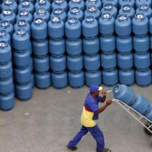 A imagem mostra uma vista aérea de um grande pátio de distribuição com centenas de botijões de gás de cozinha azuis empilhados em fileiras.