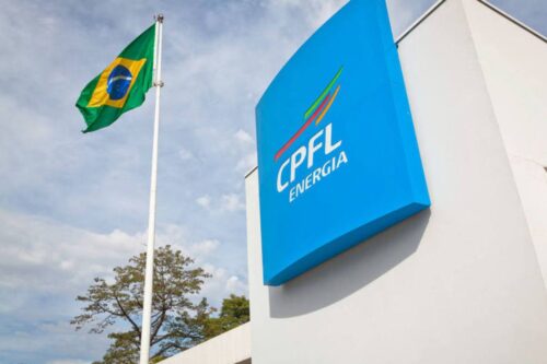 Vista de baixo de um prédio moderno branco, com a placa azul vertical da empresa CPFL Energia fixada na parede.