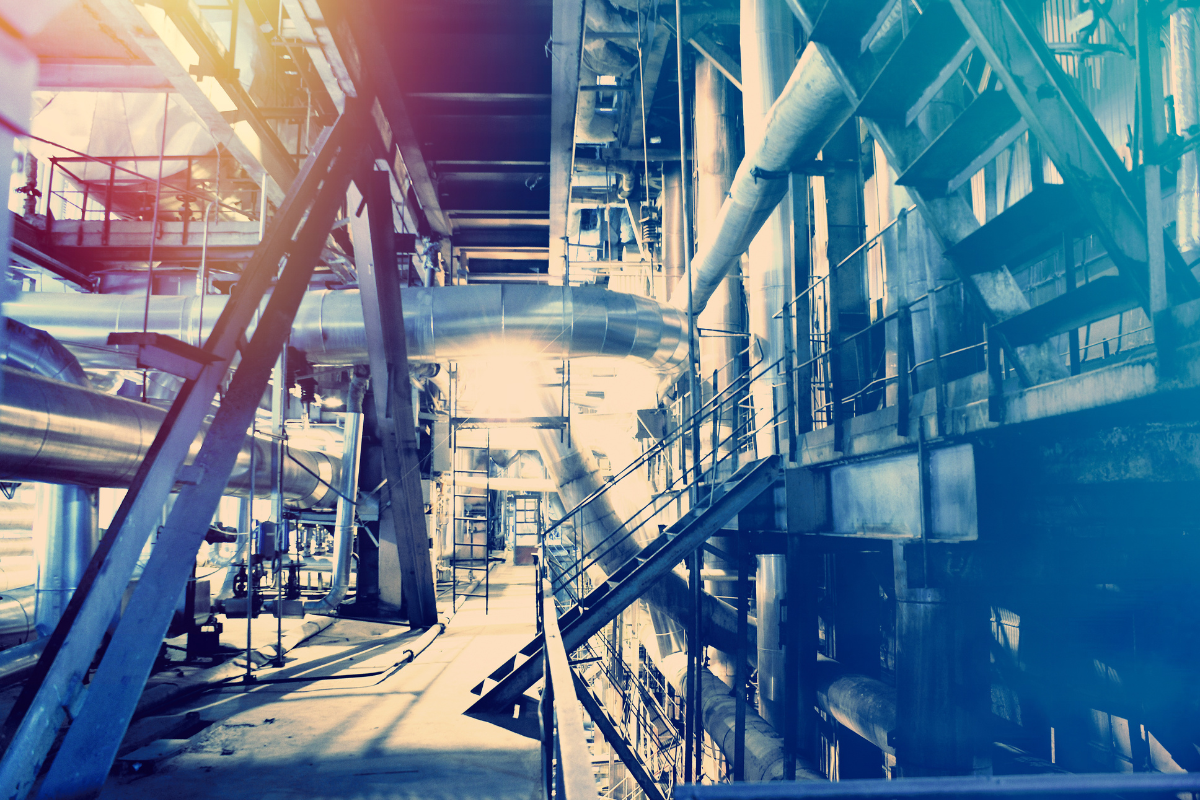 Imagem de uma zona industrial mostrando grandes tubos de aço, estruturas metálicas e escadas de acesso, com iluminação natural entrando pela parte superior.