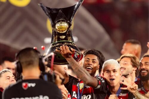 O jogador Bruno Henrique, do Flamengo, ergue sorridente o troféu do Campeonato Brasileiro (Brasileirão).