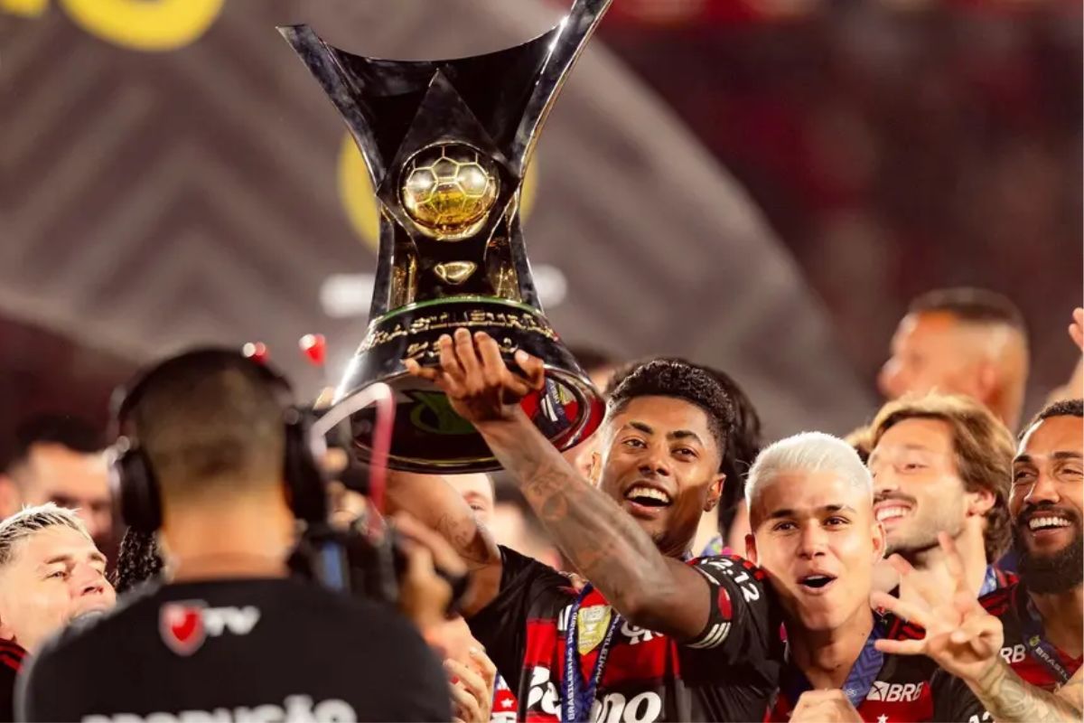 O jogador Bruno Henrique, do Flamengo, ergue sorridente o troféu do Campeonato Brasileiro (Brasileirão).
