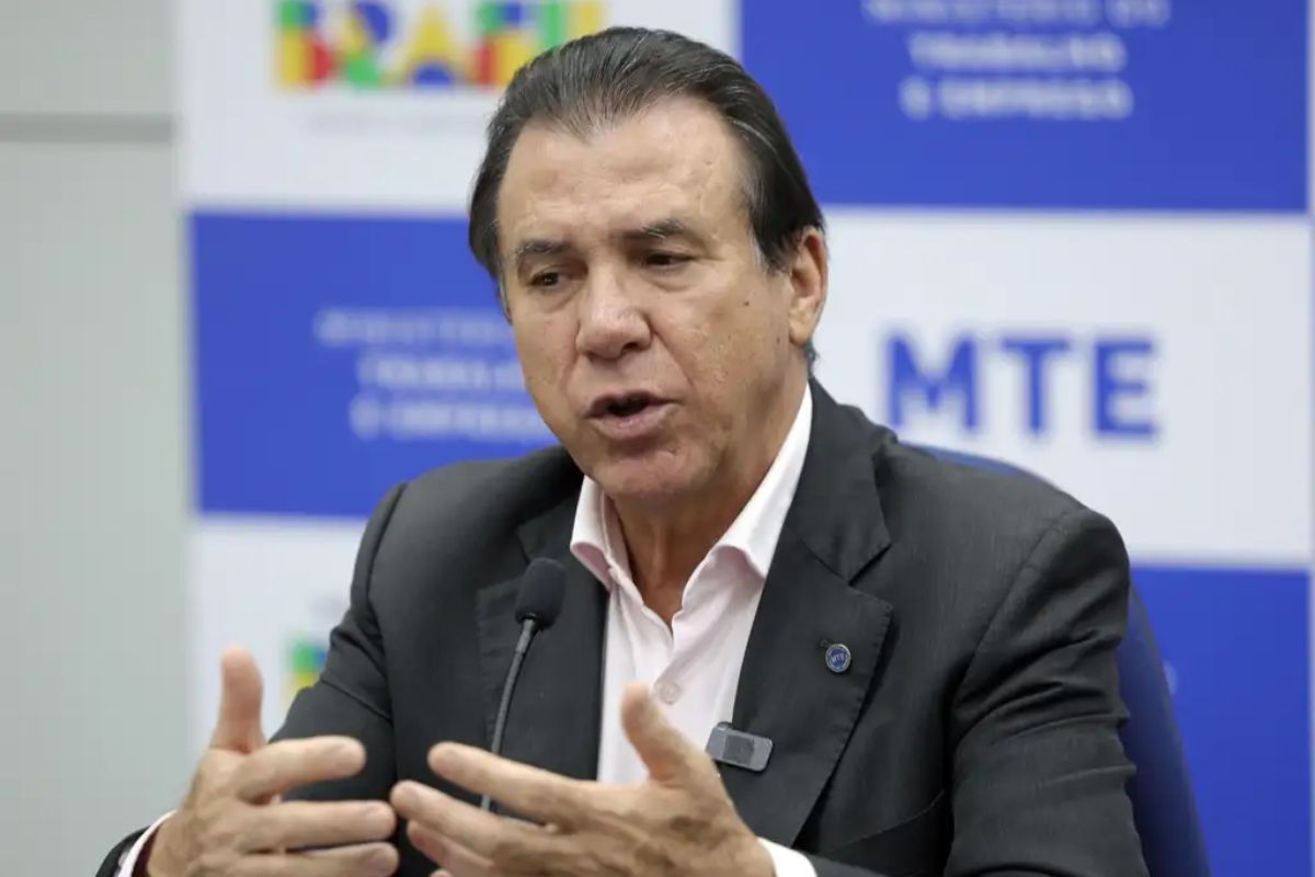 O ministro do Trabalho e Emprego, Luiz Marinho, em destaque, falando e gesticulando com as mãos durante uma coletiva ou evento.