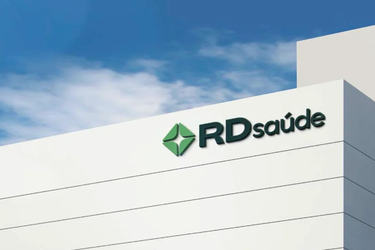 Detalhe do topo de um prédio moderno branco, com a logomarca da RD Saúde (Raia Drogasil) em relevo.
