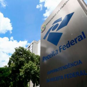 Vista de baixo para cima (contra-plongée) do letreiro da Superintendência da Receita Federal do Brasil, com o logotipo azul escuro em uma estrutura metálica vertical.