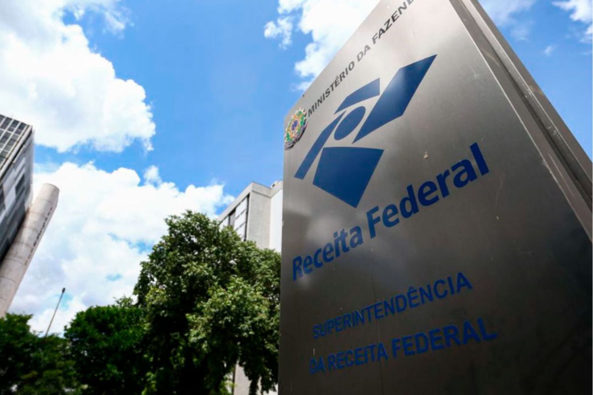 Vista de baixo para cima (contra-plongée) do letreiro da Superintendência da Receita Federal do Brasil, com o logotipo azul escuro em uma estrutura metálica vertical.