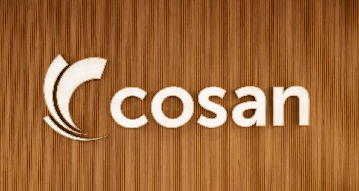 Logo da Cosan em destaque em parede de madeira, representando a holding brasileira do setor de energia, logística e combustíveis.