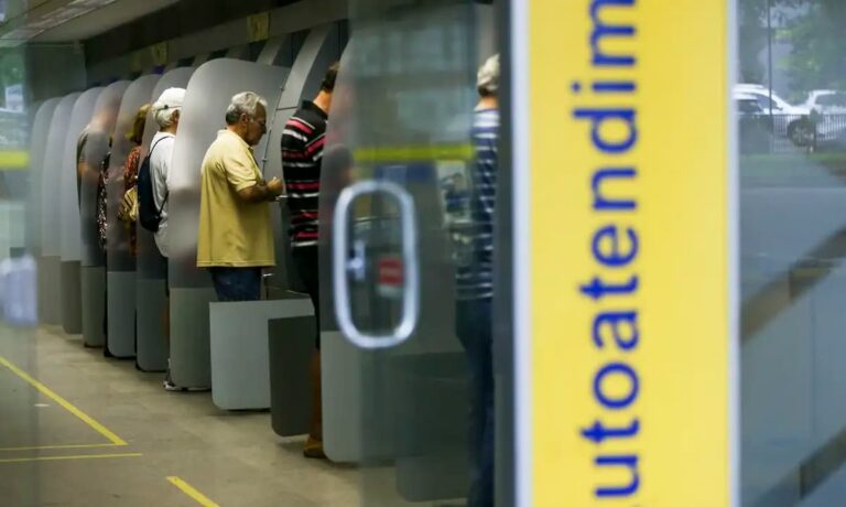 Clientes em caixas eletrônicos de agência bancária, ilustrando o funcionamento dos bancos no Natal.