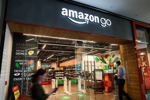 Fachada de uma loja Amazon Go com letreiro iluminado em branco sobre um painel cinza escuro.