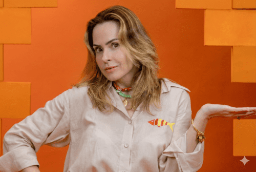 Mulher de pele clara e cabelos loiros médios ondulados, identificada como Ana Paula Renault, posando contra um fundo laranja vibrante com texturas geométricas.