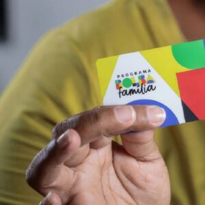 Uma pessoa segura, em primeiro plano, o cartão do novo "Programa Bolsa Família".