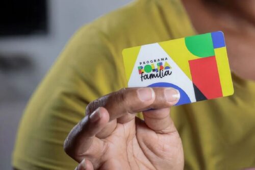 Uma pessoa segura, em primeiro plano, o cartão do novo "Programa Bolsa Família".
