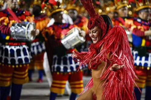Atriz Paolla Oliveira com uma fantasia de Carnaval vermelha luxuosa e brilhante desfila à frente de uma bateria da Grande Rio.